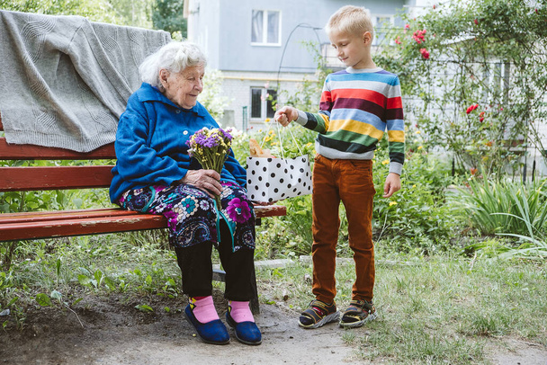 El nieto le da una flor a la abuela. El nieto y la abuela pasan tiempo juntos. Abuela con nietos disfrutando de tiempo juntos al aire libre. - Foto, Imagen