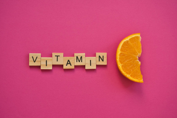 Sana C-vitamiini puisilla kirjaimilla C kuuma vaaleanpunainen tausta. Käsite ehkäisy vilustumista ja antioksidantti vitamiini. Tuore appelsiiniviipale. - Valokuva, kuva