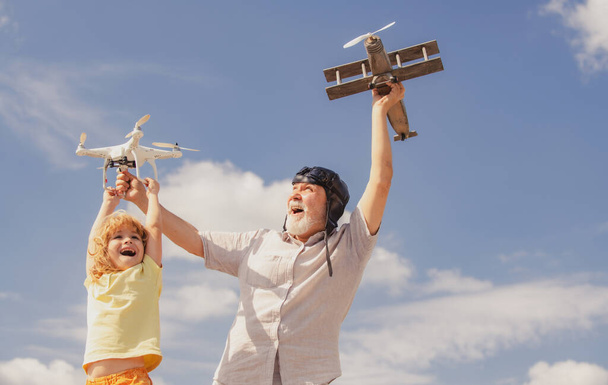 Grandfather and son playing with toy plane and quadcopter drone against sky. Child pilot aviator with plane dreams of traveling - Foto, Imagen