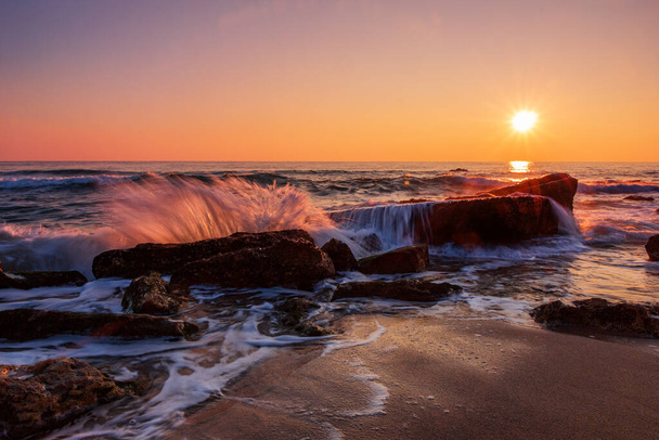 Pastelowy wschód słońca nad skalistą morską plażą. Rozmycie ruchu - Zdjęcie, obraz