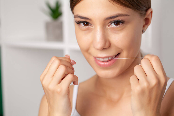 Uśmiechnięte kobiety używają nici dentystycznej białe zdrowe zęby - Zdjęcie, obraz