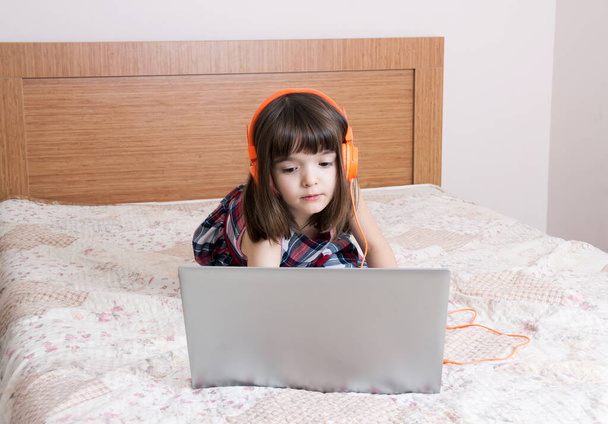Маленька дівчинка використовує ноутбук з навушниками
 - Фото, зображення
