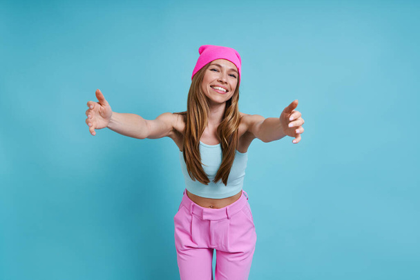 Happy young woman in pink hat smiling while standing against blue background - Photo, Image