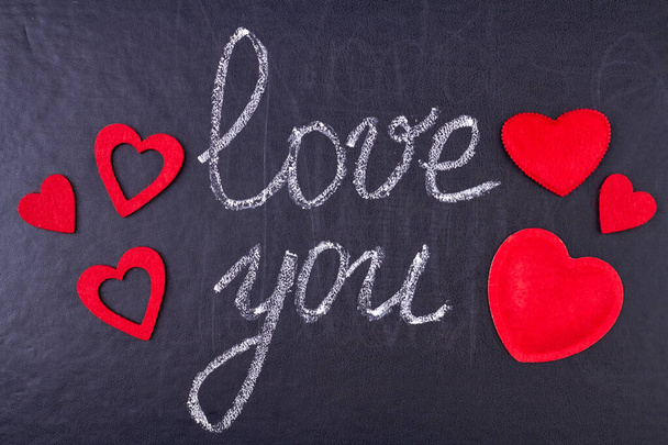 Handgeschreven krijtinscriptie Ik hou van je op zwart krijtbord met rode decoratieve hartjes. Boodschap van de liefde. - Foto, afbeelding