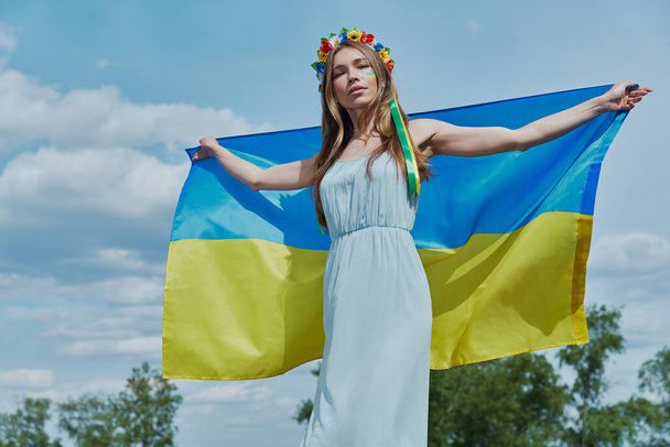 Confident young Ukrainian woman holding national flag with sky in the background - Valokuva, kuva