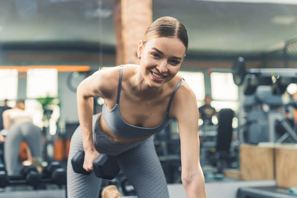 Mujer en forma haciendo ejercicio con pesas de mancuerna en el banco del gimnasio y sonriendo a la cámara durante el día. Foto de alta calidad - Foto, Imagen