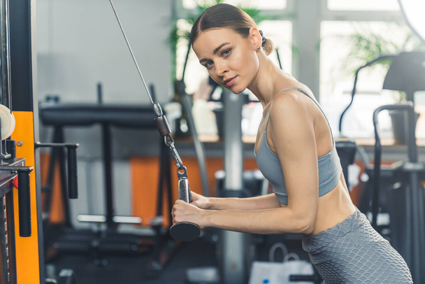 Fitness mulher caucasiana fazendo exercícios tríceps no ginásio e olhando para a câmera. Foto de alta qualidade - Foto, Imagem