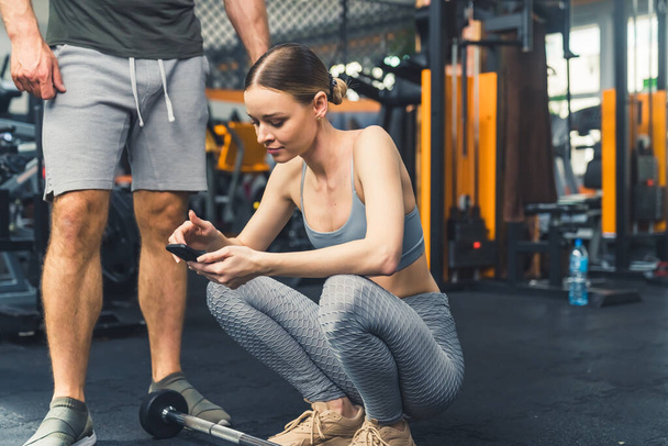 Una bella ragazza in un cappotto sportivo grigio controlla la correttezza di un esercizio sul suo telefono in palestra. Foto di alta qualità - Foto, immagini