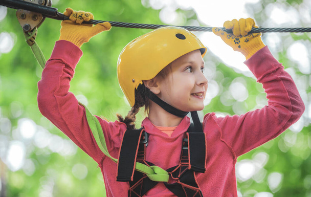 Portrait of a beautiful kid on a rope park among trees. Happy child in summer. Roping park. Rope park - climbing center. Toddler age. Kid climbing trees in park. Every childhood matters - Foto, Bild