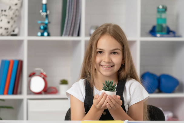Счастливый ребенок держит горшечное растение в школьном классе. - Фото, изображение