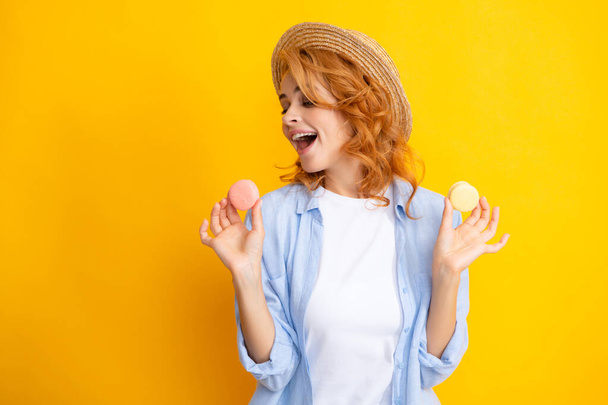 Young woman eating delicious macaroon on yellow background. Girl eat the macaron - Photo, Image