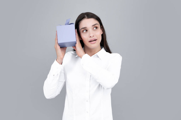 Attractive woman with present box posing with surprised face expression on gray background. Girl holding gift decorated with ribbon. Valentine day, birthday, happy new year gift people concept - Valokuva, kuva
