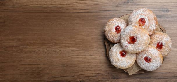 Delicious donuts with jelly and powdered sugar on wooden table, top view. Space for text - Photo, image
