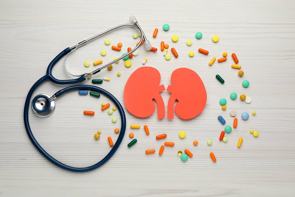 Paper cutout of kidneys, stethoscope and pills on white wooden table, flat lay - Photo, Image