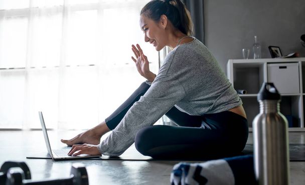 Sporty young Asian woman exercising at home, watching fitness video on Internet or having online fitness class, using laptop, living room interior, copy space - Photo, Image