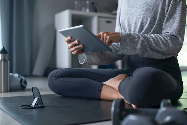 Sporty young Asian woman exercising at home, watching fitness video on Internet or having online fitness class, using tablet , living room interior, copy space - Valokuva, kuva