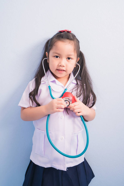 Szczęśliwe słodkie dziewczyny w białym mundurze medycznym i stetoskop działać jak lekarz. dziecko marzy o zostaniu lekarzem koncepcja kariery. - Zdjęcie, obraz