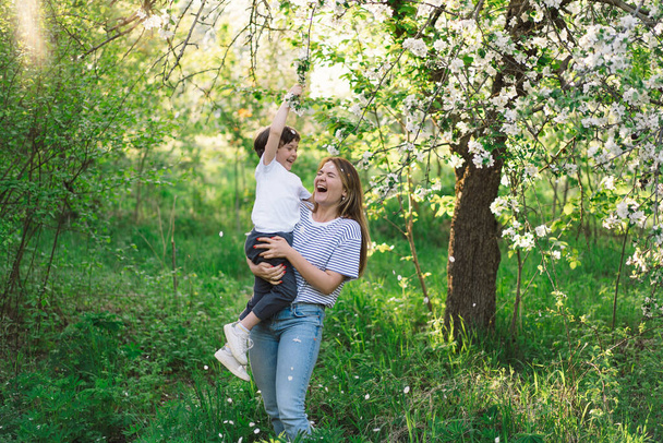 Mother with little baby son in spring garden during golden hour. Mom and son are active in nature. Family walks in a spring garden. Happy mothers day - Fotografie, Obrázek