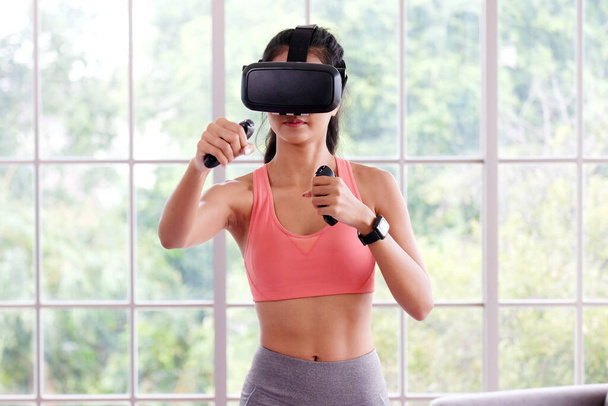 Asyalı kadın sanal gerçeklik kulaklığı evde egzersiz yaparken sağlıklı Asyalı kız interaktif egzersiz, spor, kadın ve giyilebilir teknoloji için VR gözlük takıyor. - Fotoğraf, Görsel