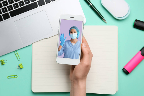 Woman holding smartphone with doctor on screen at table, top view. Concept of telemedicine - Photo, Image