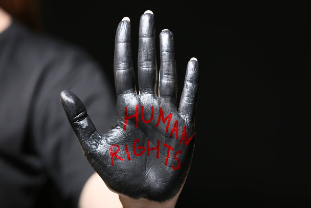 Woman with paint and text HUMAN RIGHTS on her palm against dark background, closeup - Foto, immagini