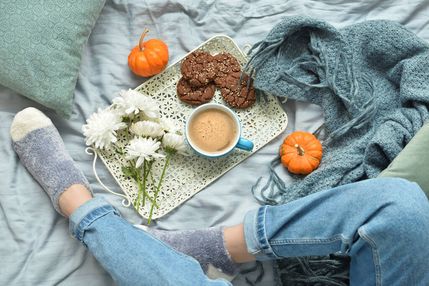 Patas femeninas con hermosas flores de crisantemo y taza de sabroso café de calabaza en la cama - Foto, Imagen