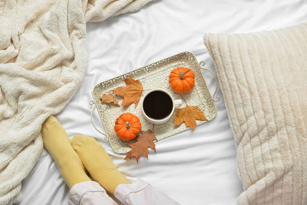Female legs and cup of tasty pumpkin coffee on bed - Photo, Image