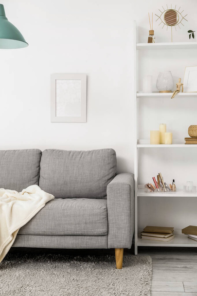 Сірий диван з пледом і стелажем біля світлої стіни
 - Фото, зображення