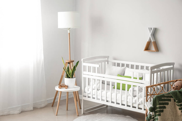 Interior of light nursery with baby crib, lamp, table and armchair - 写真・画像