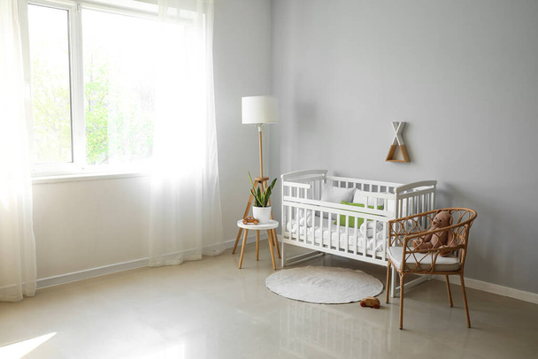 Bebek beşiği, lamba, masa ve koltuğu olan ışık odasının içinde. - Fotoğraf, Görsel
