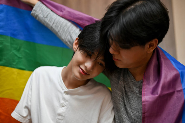 Романтична азіатська пара підлітків-геїв, чоловік поклав голову на плече свого хлопця, поділившись романтичною прихильністю. ЛГБТ веселка прапор
 - Фото, зображення