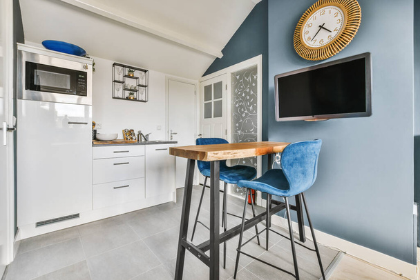 Modern minimalista stílusú belsőépítészeti stúdió apartman nyitott fehér konyha és étkező asztallal és székekkel megvilágított tetőtéri stílusú lámpa - Fotó, kép
