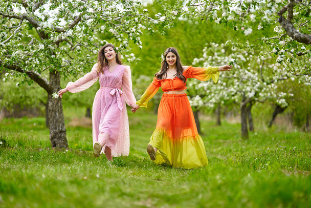 Two women of Indian and White heritage, mixed race, walking hand in hand in a blooming apple orchard - Fotoğraf, Görsel