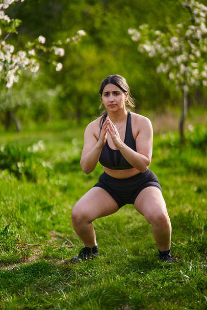 Rozmiar plus silna Hinduska kobieta robi trening fitness na świeżym powietrzu w sadzie jabłkowym - Zdjęcie, obraz
