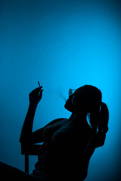 Gyönyörű sziluett egy lányról a stúdióban, aki egy kék háttér előtt ül. - Fotó, kép