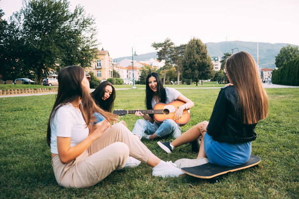 Cztery niesamowite i zabawne dziewczyny przyjaciele spędzają czas w parku i śmieją się podczas gry na gitarze - Zdjęcie, obraz