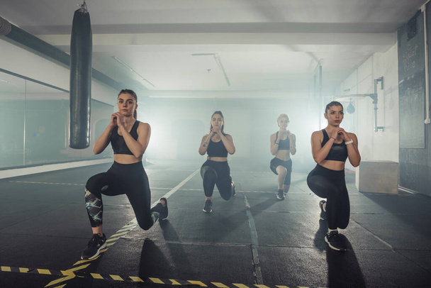 Group of sportswomen in sportswear doing lunge exercise at the gym with their right leg - Photo, Image