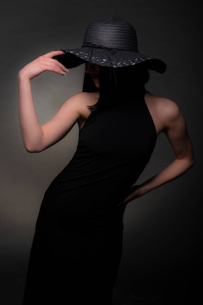Elegante Frau posiert in perfekter Struktur in schwarzem Kleid und Hut - Foto, Bild