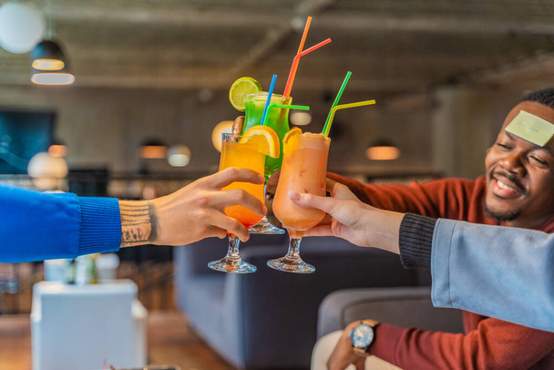 Drie multiraciale vrienden juichen met hun cocktails, close-up - Foto, afbeelding