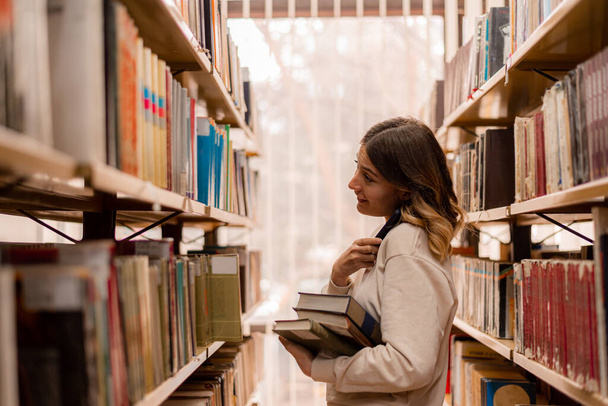 Dívka drží svůj telefon při výběru knihy z knihoven - Fotografie, Obrázek