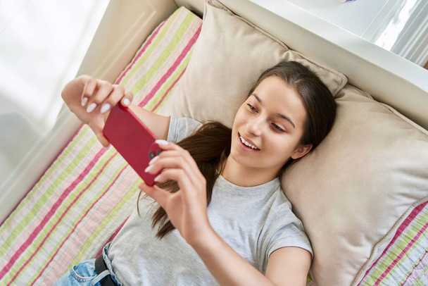 Beautiful young teenage female resting lying on couch using smartphone. Girl browsing social media, making videos for stories, shopping, chatting in network. Lifestyle, technology, home leisure - Фото, зображення