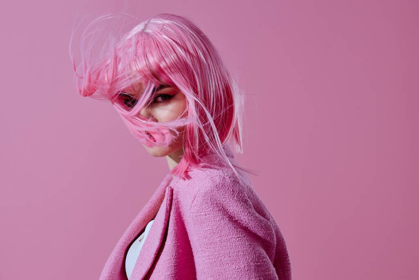 Mujer joven positiva chaqueta rosa que sostiene los cosméticos del pelo fondo rosa inalterado. Foto de alta calidad - Foto, imagen