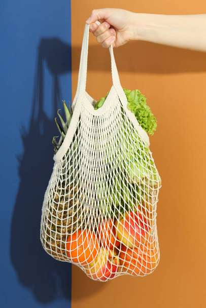 Mano femminile tiene borsa stringa con generi alimentari su sfondo bicolore - Foto, immagini