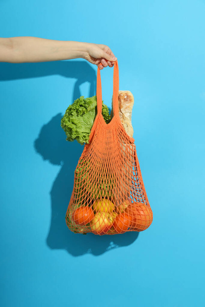 Female hand holds string bag with grocery on blue background - Zdjęcie, obraz