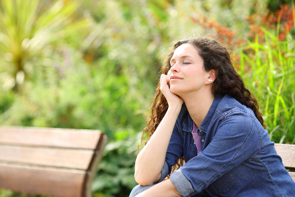 Happy woman resting with closed eyes sitting in a park - Photo, image