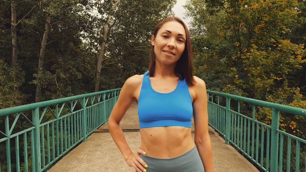 Retrato de una joven atlética asiática en un puente en la selva. Mujer en ropa deportiva - Foto, Imagen