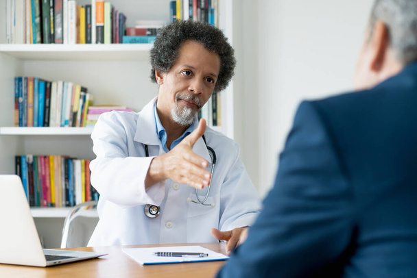 African american senior doctor congratulating patient to healthy lifestyle at office of hospitak - Foto, Bild