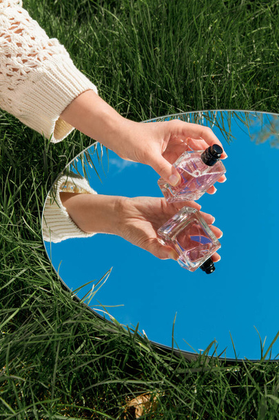 perfumery and nature concept - hand with bottle of perfume and sky reflection in round mirror on summer field - Foto, imagen