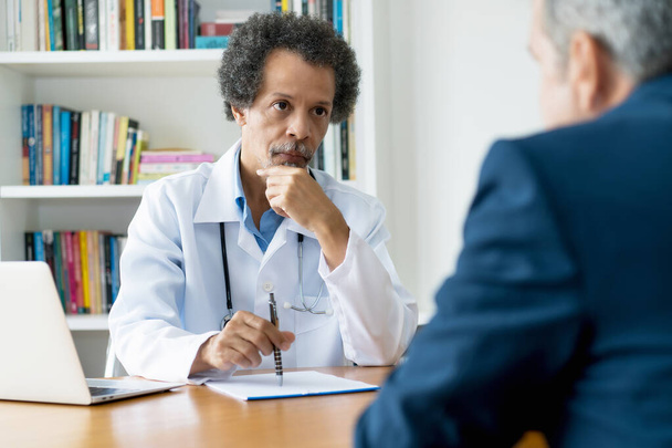 Concerned african american senior doctor listening to patient at office of hospitak - 写真・画像