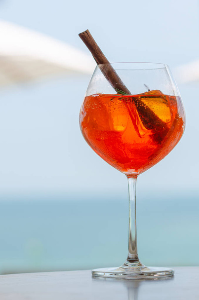 Bir bardak portakal kokteyli, bulanık şemsiye ve yaz ve yaz içeceği konsepti için deniz arka planıyla masaya konur.. - Fotoğraf, Görsel